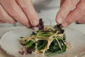 Chef finishing cold spinach salad with sesame dressing, ginger and shiso